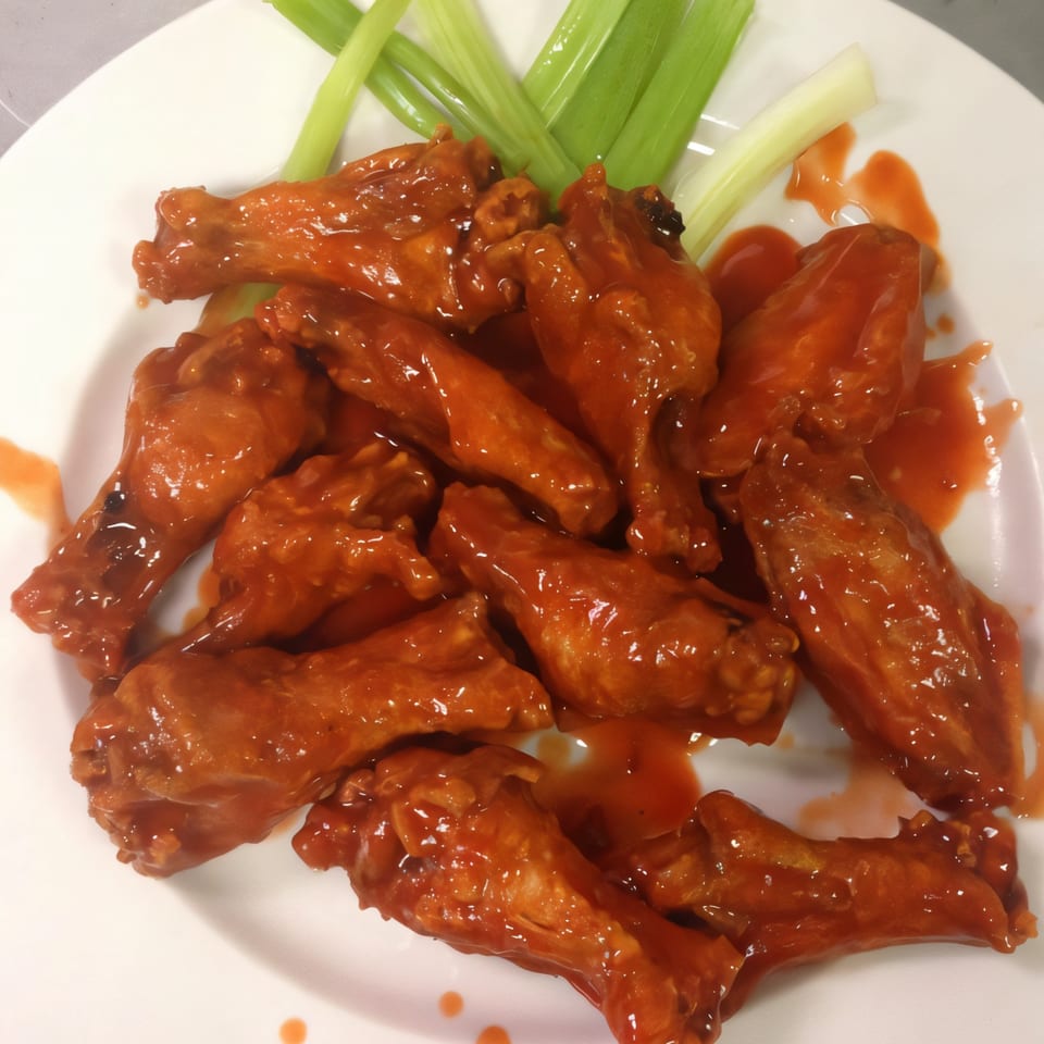 A plate of Medo's Italian Restaurant's buffalo wings, coated in red sauce, with celery sticks.