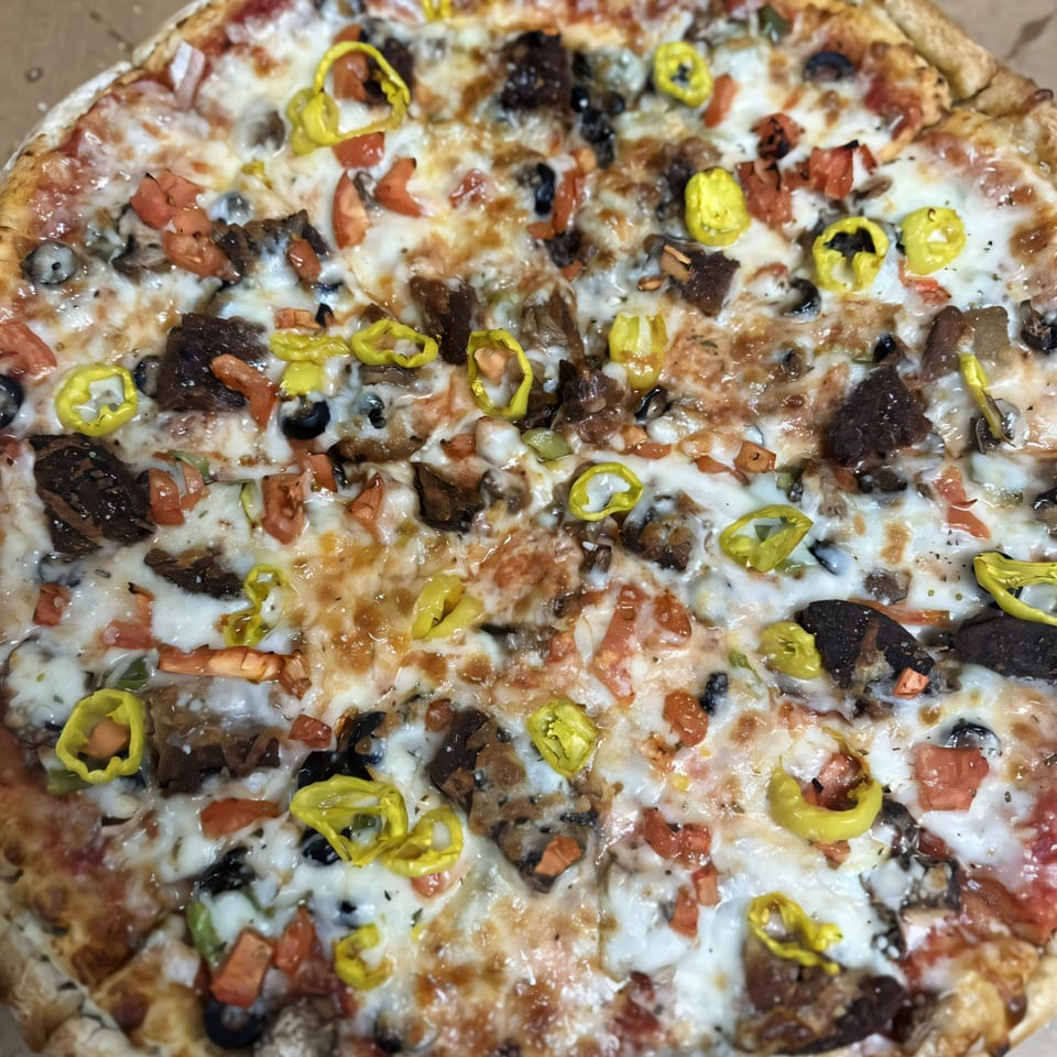 Close-up of a Medo's Italian Restaurant pizza with melted cheese, tomatoes, olives, and banana peppers.