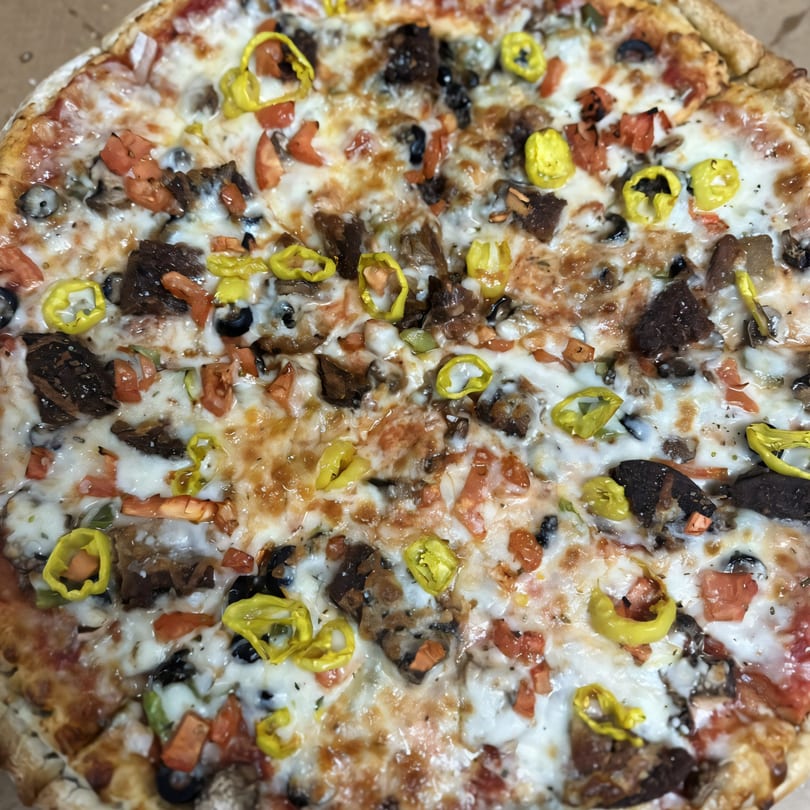 Close-up of a Medo's Italian Restaurant pizza with melted cheese, tomatoes, olives, and banana peppers.